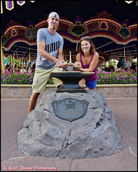 A young couple tries to pull the sword from the stone in front of Prince Charming Regal Carrousel at the Magic Kingdom, Walt Disney World, Orlando, Florida